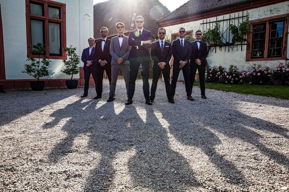 Bräutigam und Freunde in Anzügen mit Sonnenbrillen, lange Schatten auf Kies