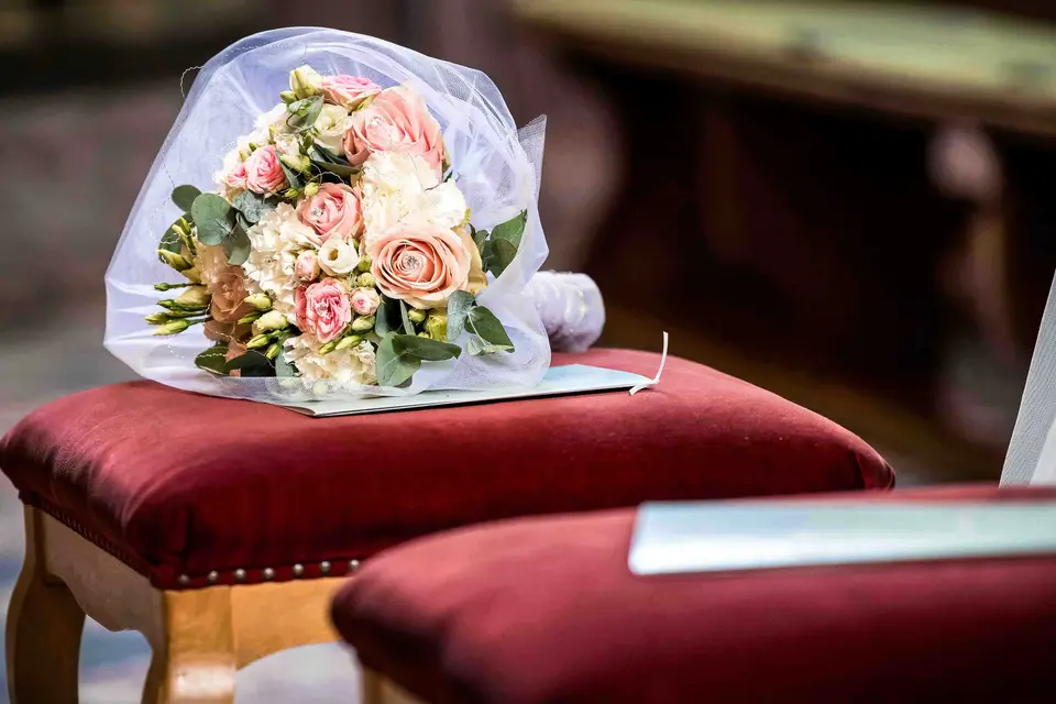 Brautstrauß mit Rosen liegt auf einem roten Samthocker