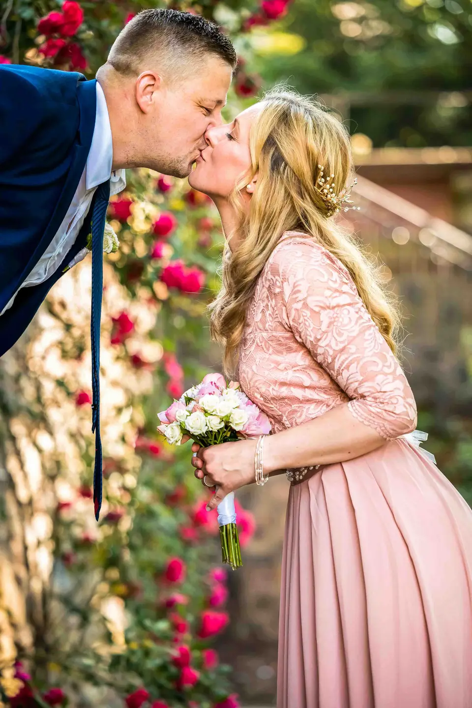 Brautpaar küsst sich vor blühenden Rosen im Garten