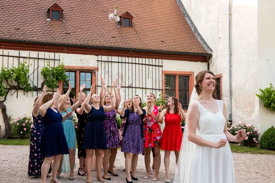 Braut wirft den Brautstrauß, Freundinnen strecken die Arme aus
