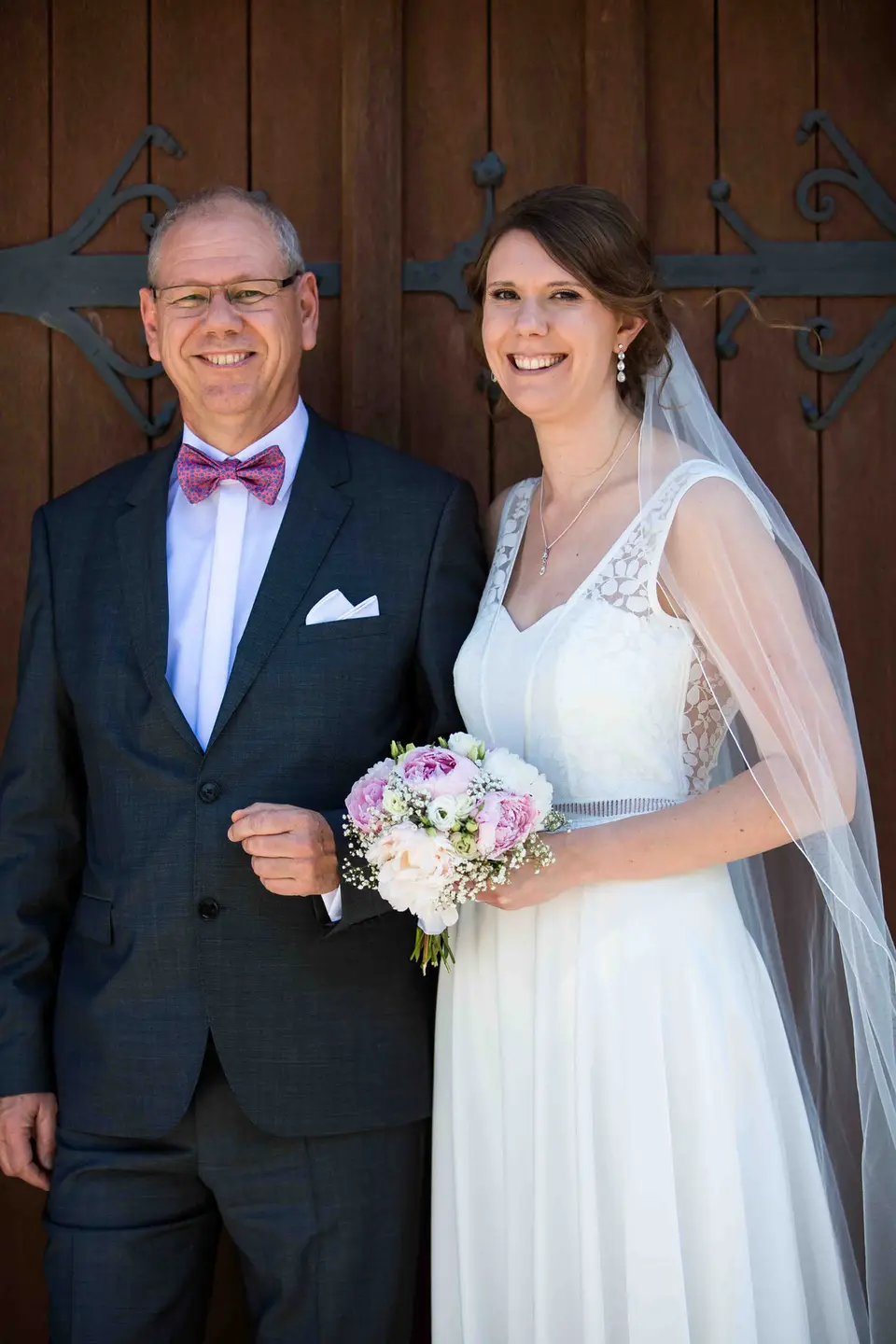 Braut mit ihrem Vater vor einer dunklen Holztür