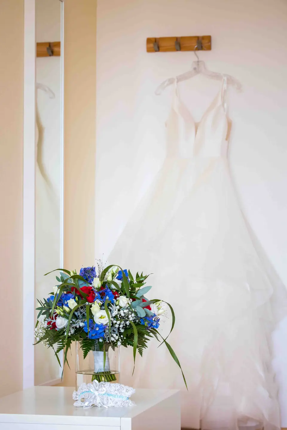 Brautkleid am Bügel neben einem Strauß in Blau, Weiß und Rot