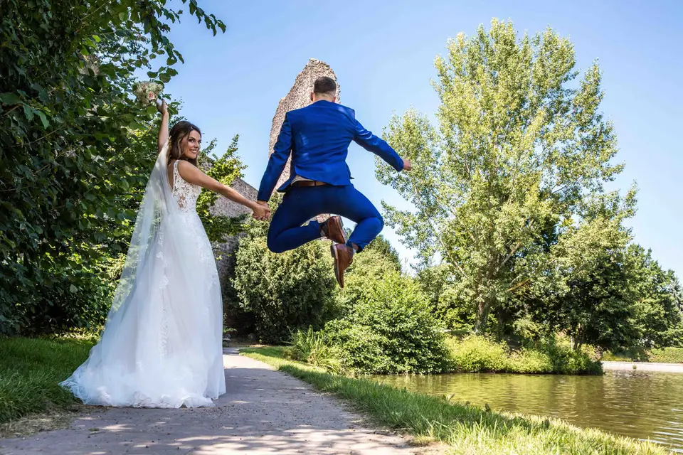 Bräutigam springt hoch, Braut hält seine Hand am Wasser