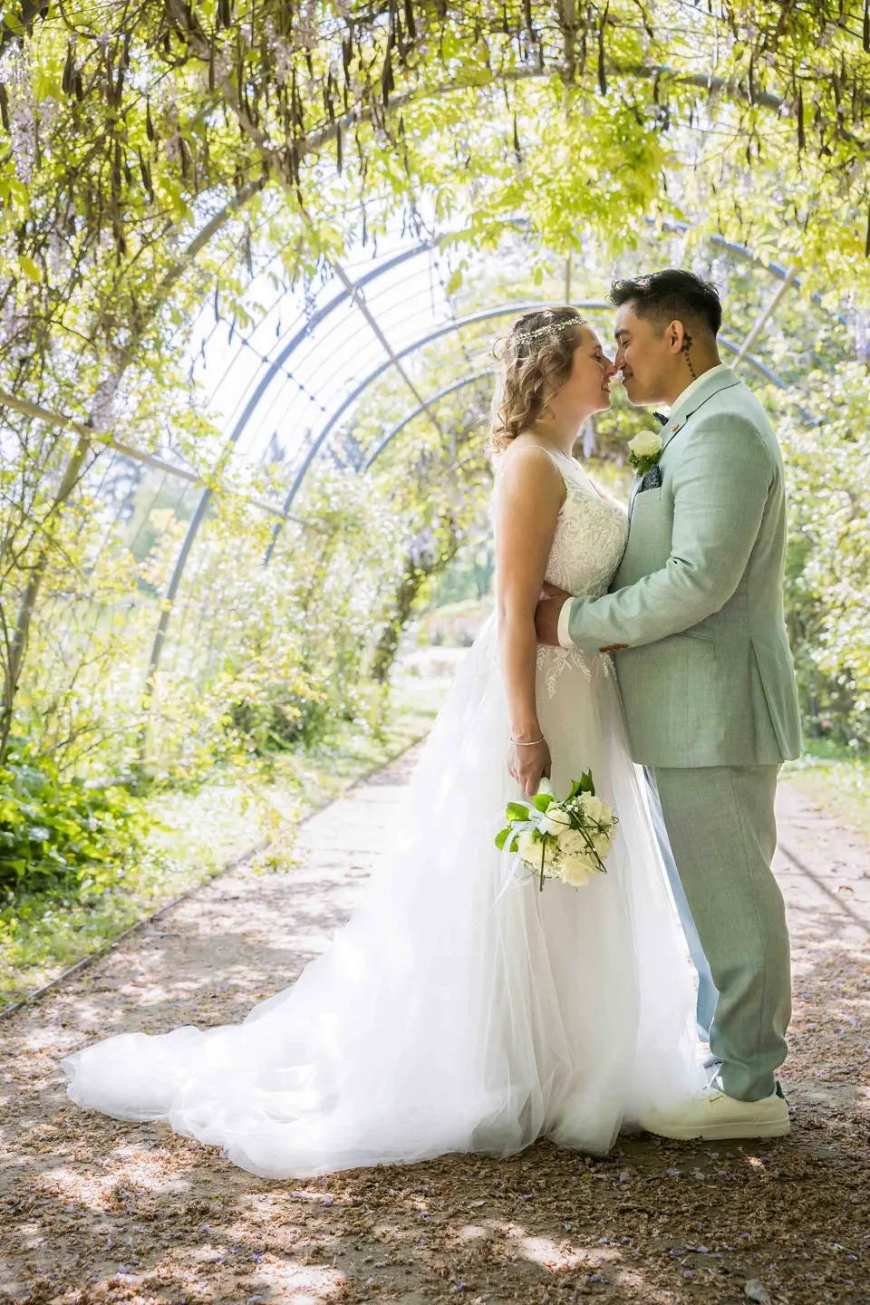 Brautpaar umarmt sich unter einem Rosenbogen im Rosarium
