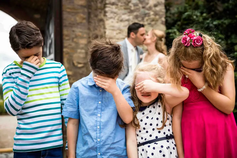 Kinder halten sich die Augen zu, während das Brautpaar sich küsst