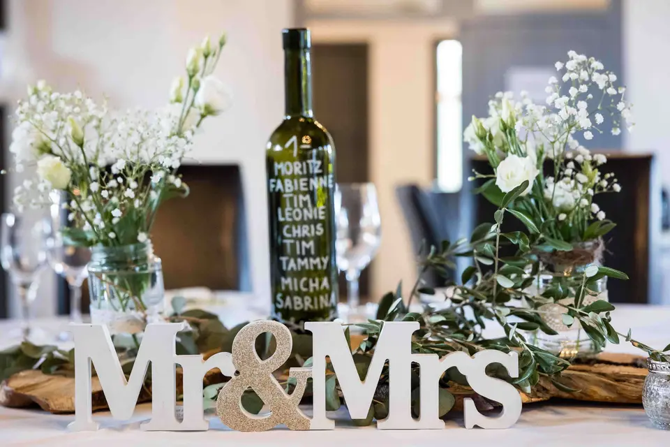Tischdeko mit Mr & Mrs Schriftzug, Weinflasche und weißen Blumen