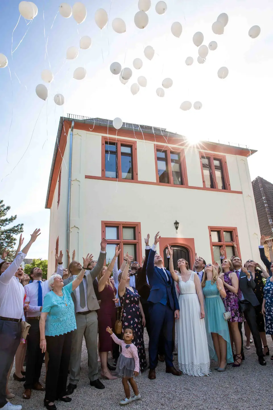 Gruppenbild der Hochzeitsgesellschaft mit weißen Luftballons vor dem Haus