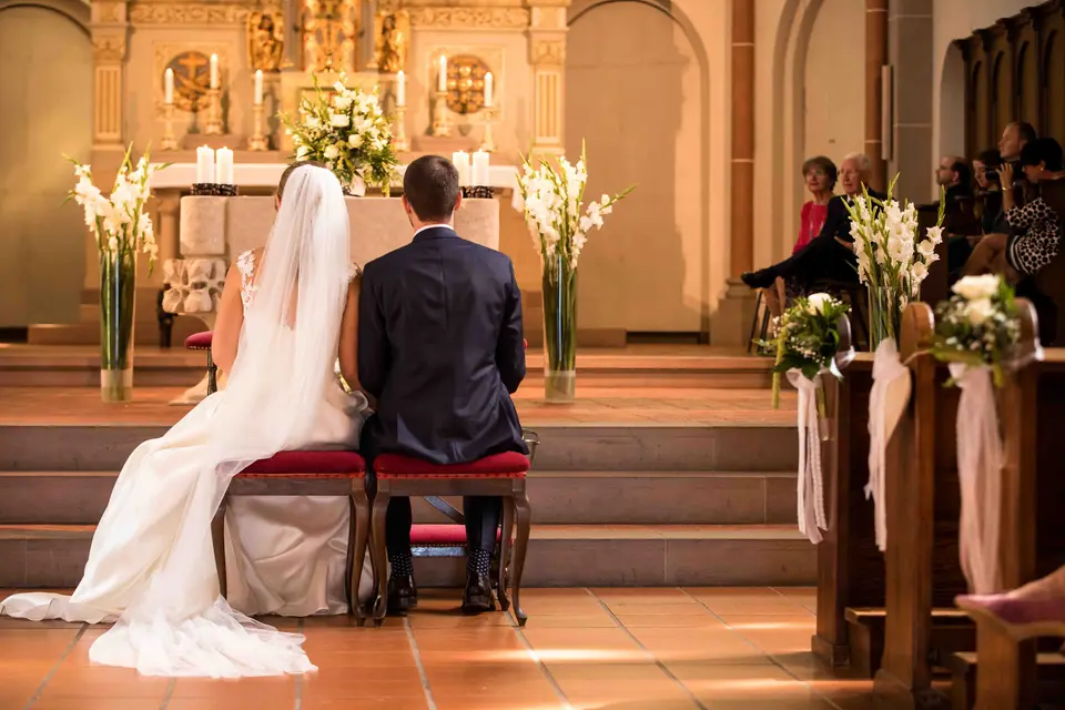 Brautpaar kniet von hinten gesehen vor dem geschmückten Altar