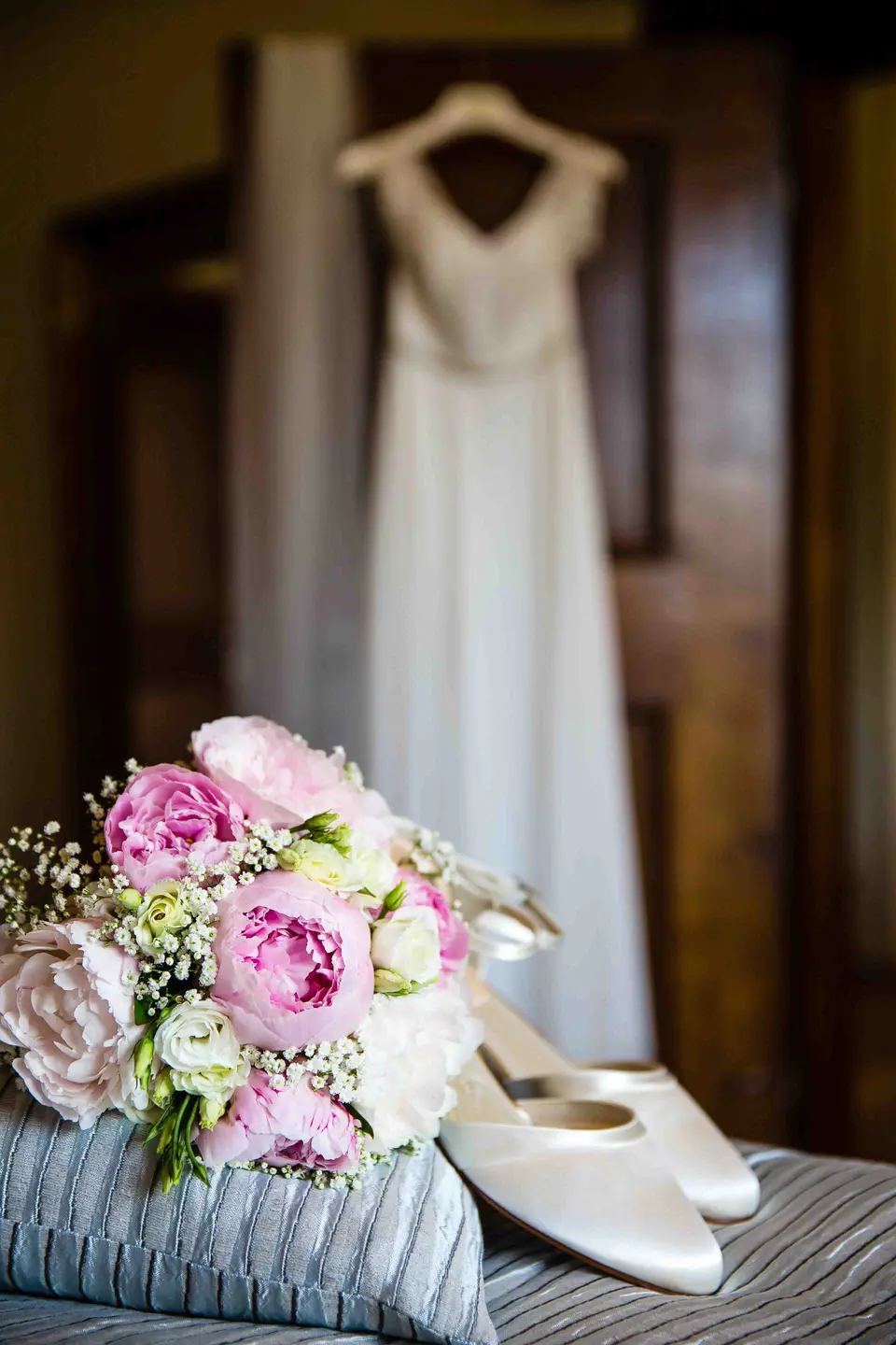 Brautkleid am Bügel, davor Brautschuhe und rosa Brautstrauß