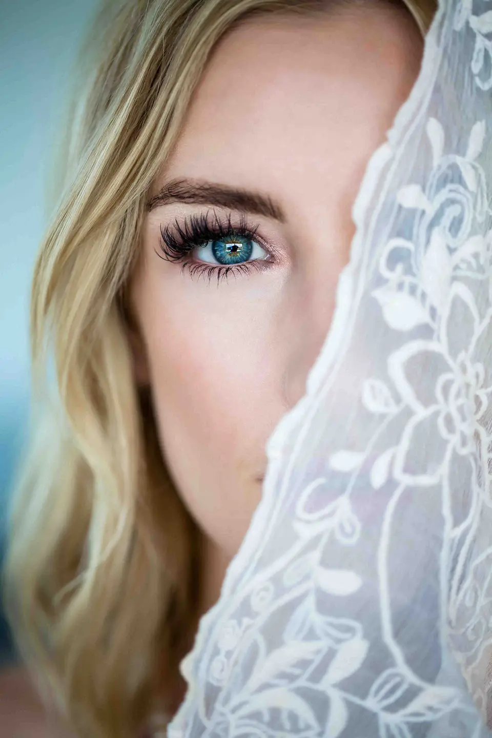 Braut mit blauen Augen blickt hinter einem Spitzenschleier hervor