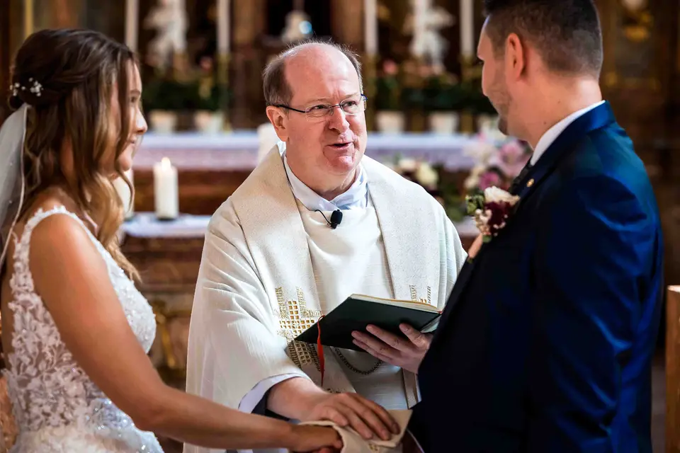 Pfarrer segnet die Ringe, Braut und Bräutigam stehen vor dem Altar