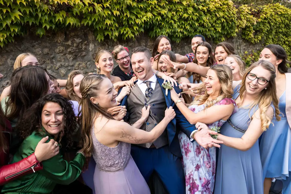 Freundinnen umringen den Bräutigam lachend für ein Gruppenbild