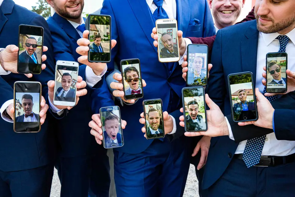 Männer im Anzug halten Handys mit lustigen Gesichtern in die Kamera