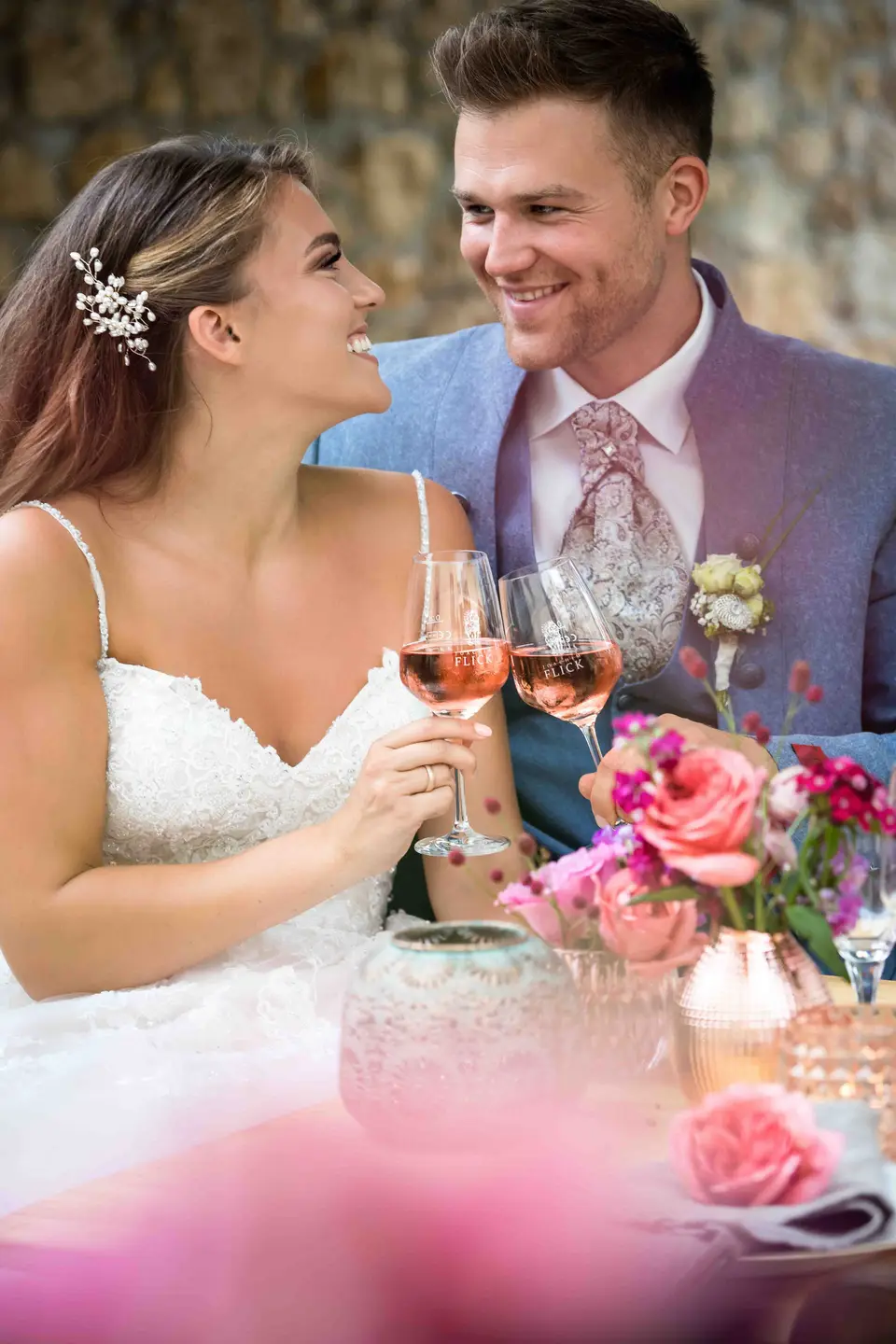 Brautpaar stößt an einem Tisch mit Blumen mit Roséwein an