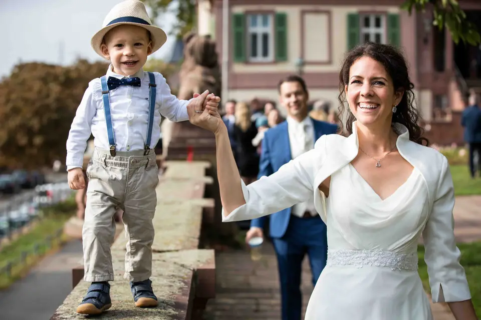 Braut hält einen kleinen Jungen auf einer Mauer an der Hand