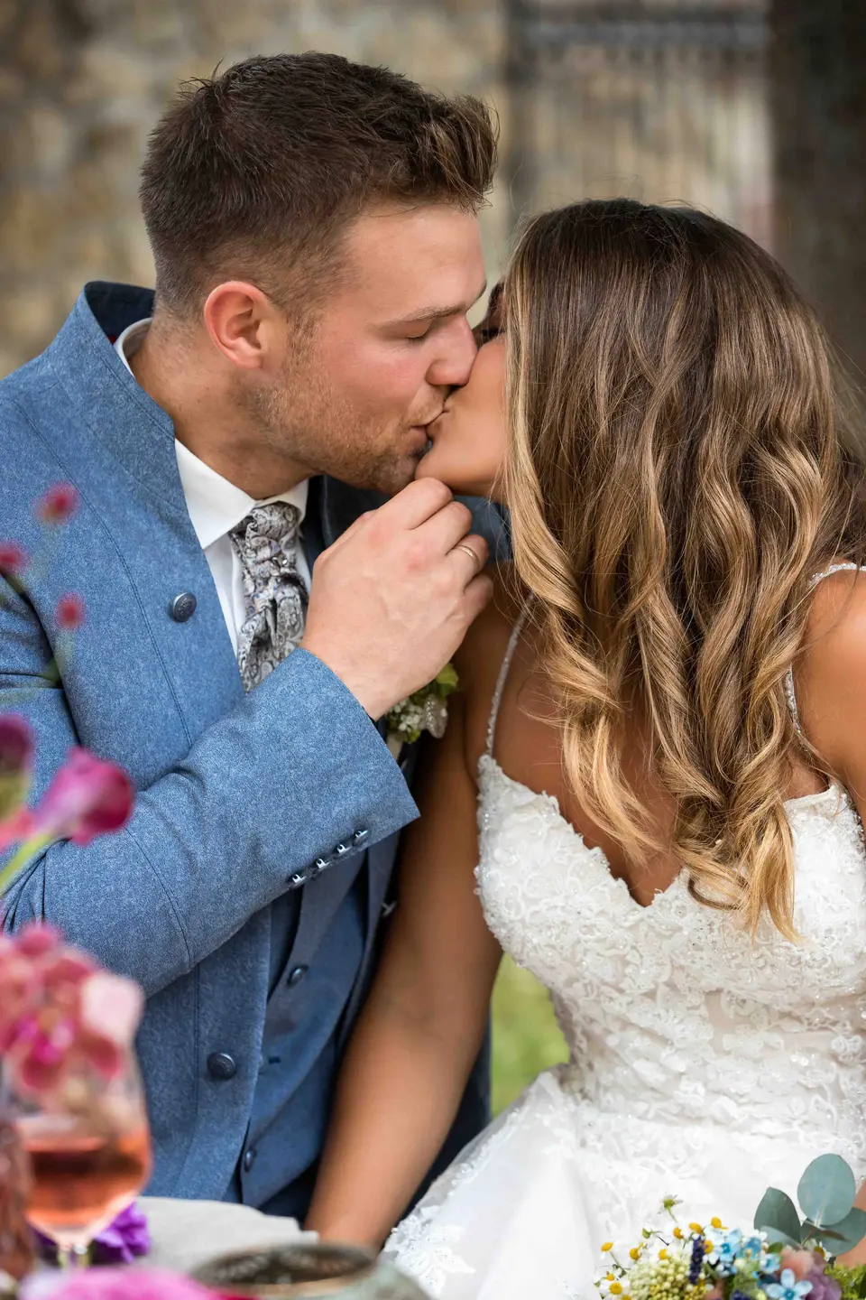 Brautpaar küsst sich an der gedeckten Hochzeitstafel