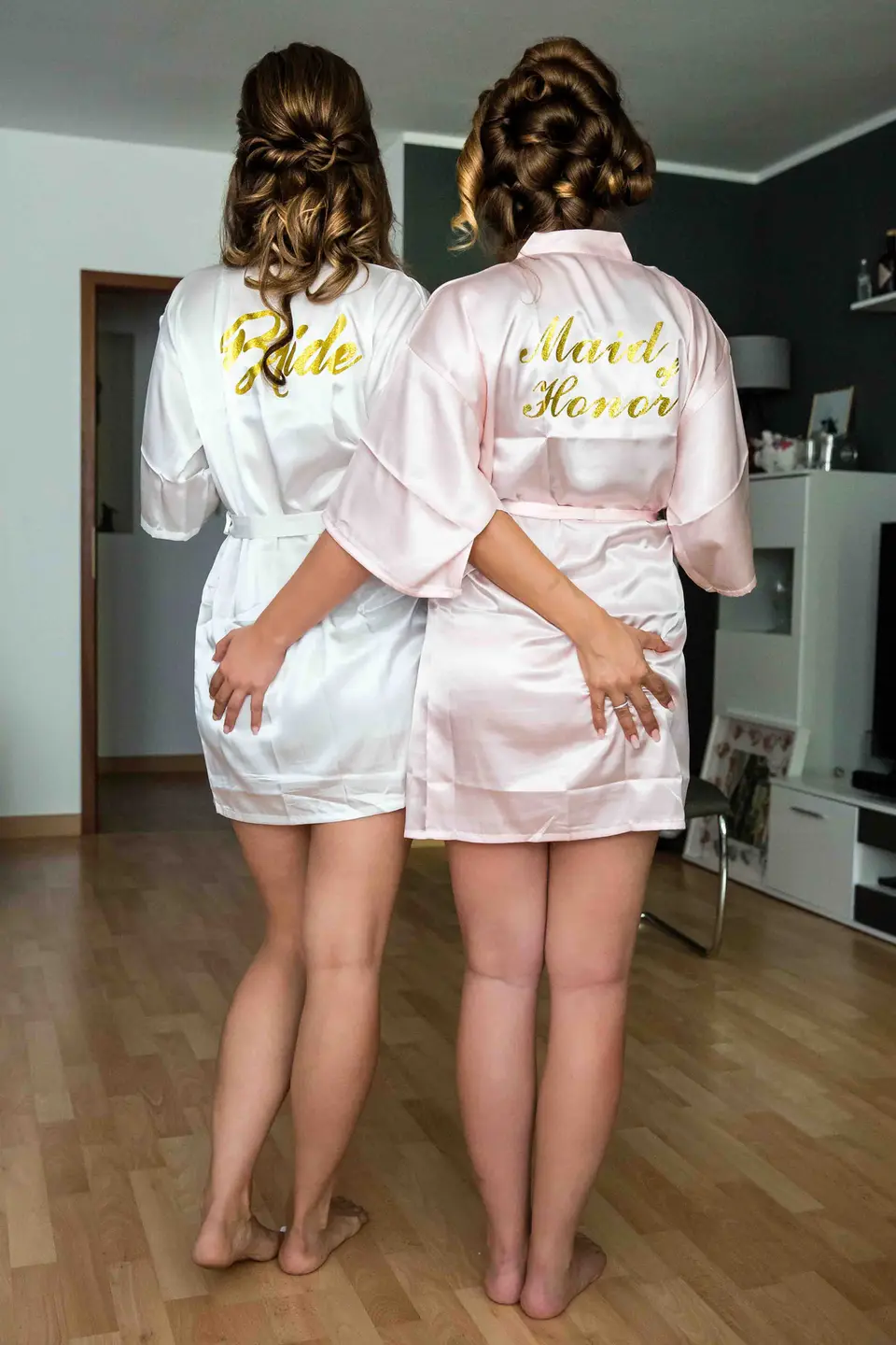 Braut und Trauzeugin in Morgenmänteln von hinten, Arm in Arm