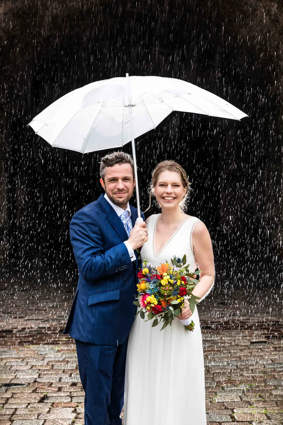 Brautpaar unter einem weißen Schirm im Regen