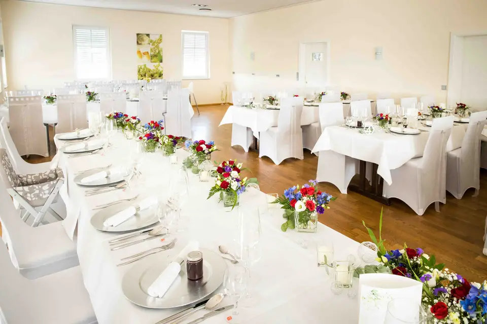 Festsaal mit weiß eingedeckten Tafeln und bunten Blumen