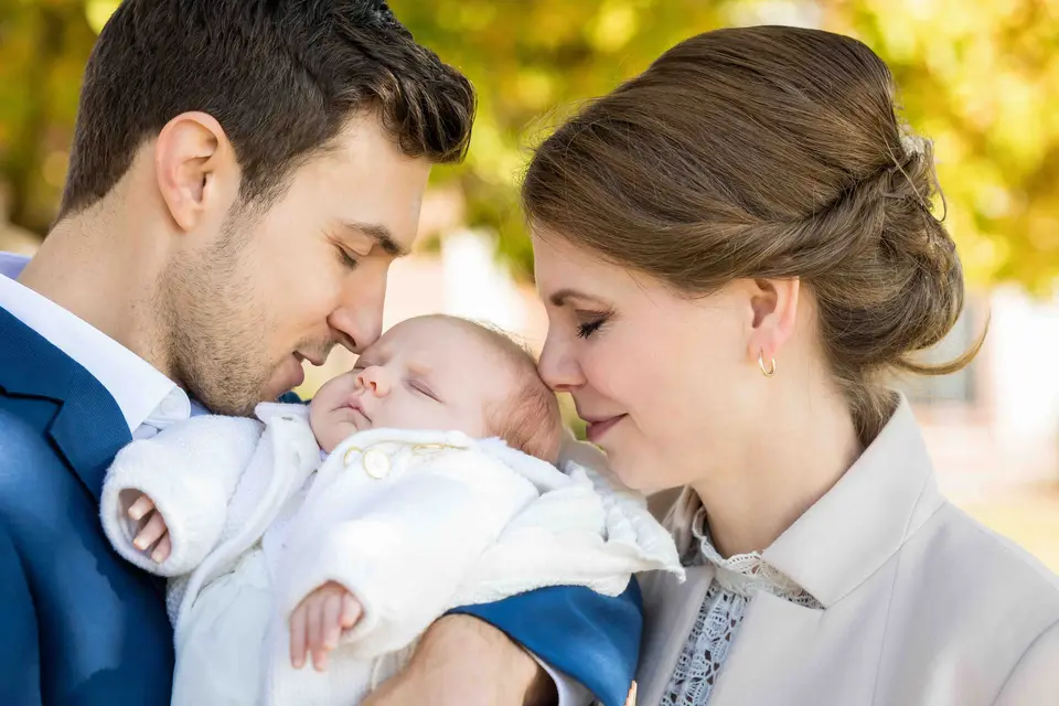 Brautpaar mit Baby im Arm, die Gesichter ganz nah beieinander