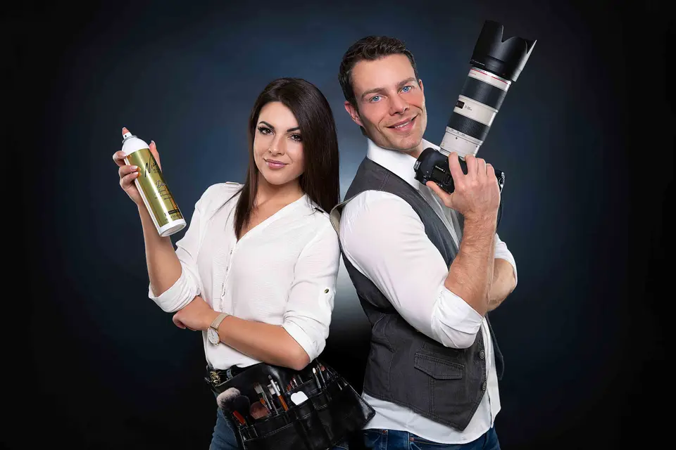 Stylistin mit Haarspray und Fotograf mit Kamera stehen Rücken an Rücken