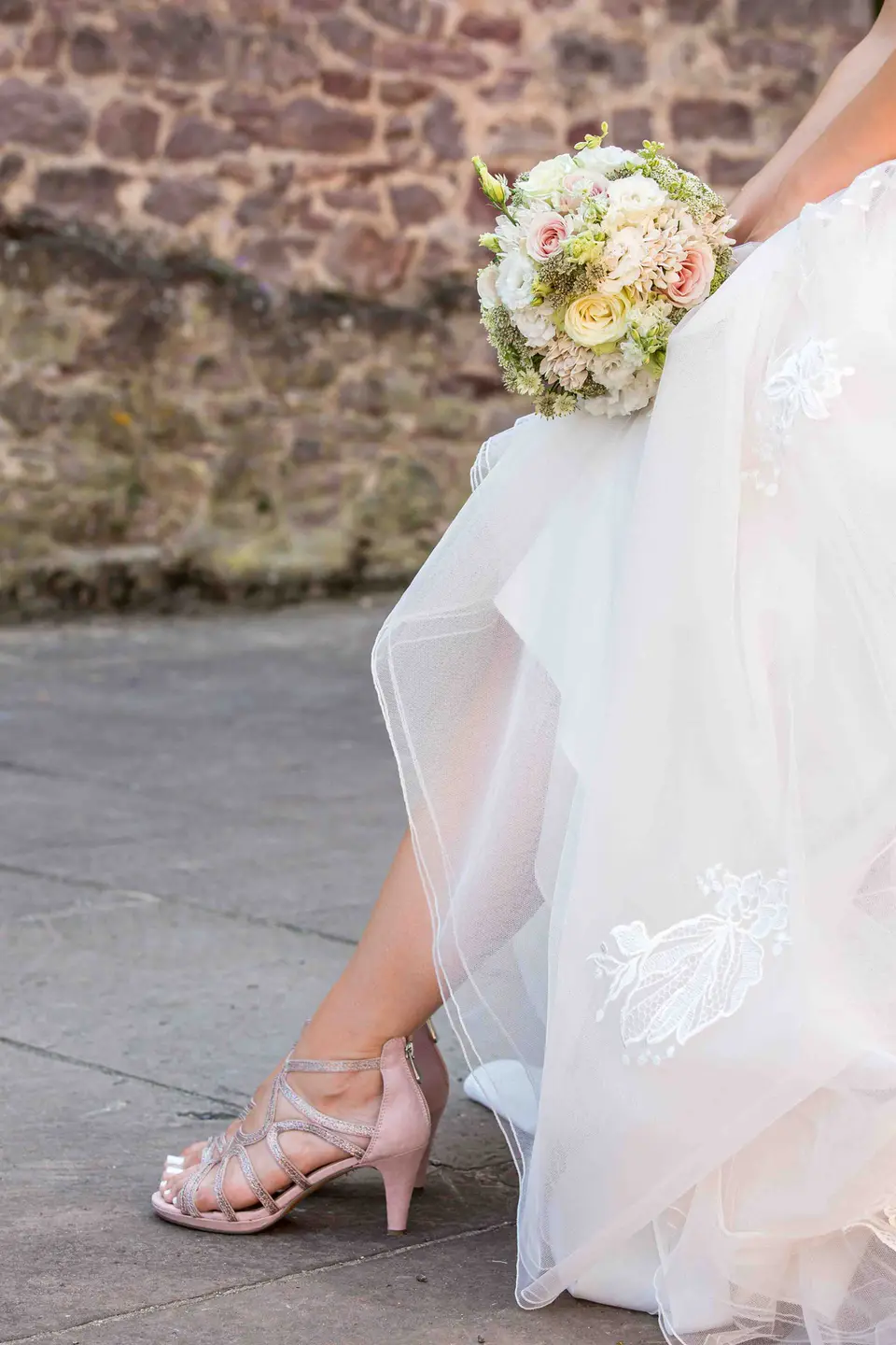 Braut rafft das Kleid und zeigt die Brautschuhe