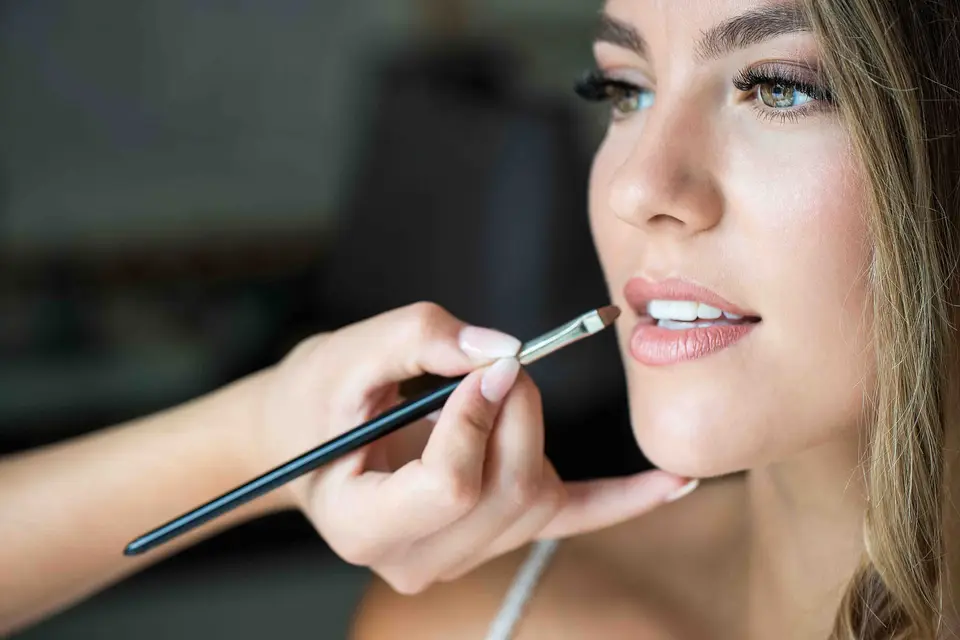 Braut bekommt Lippenfarbe mit dem Pinsel aufgetragen