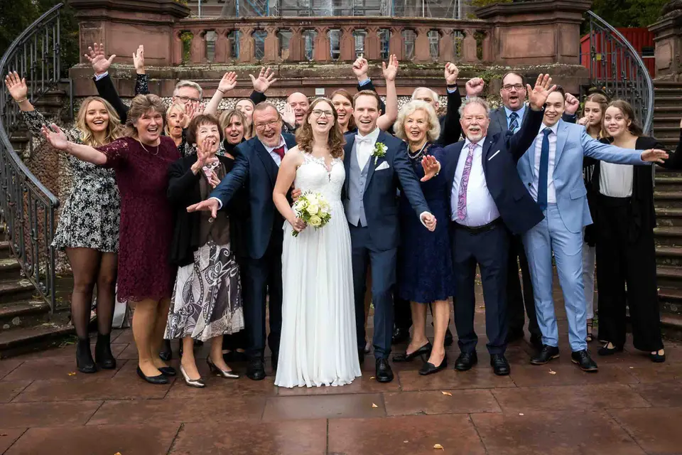 Gruppenbild mit Brautpaar und jubelnden Gästen vor der Treppe