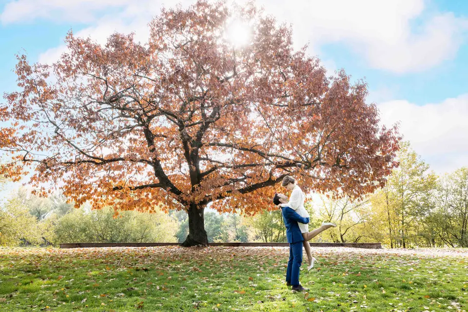 Bräutigam hebt die Braut unter einem großen Herbstbaum hoch