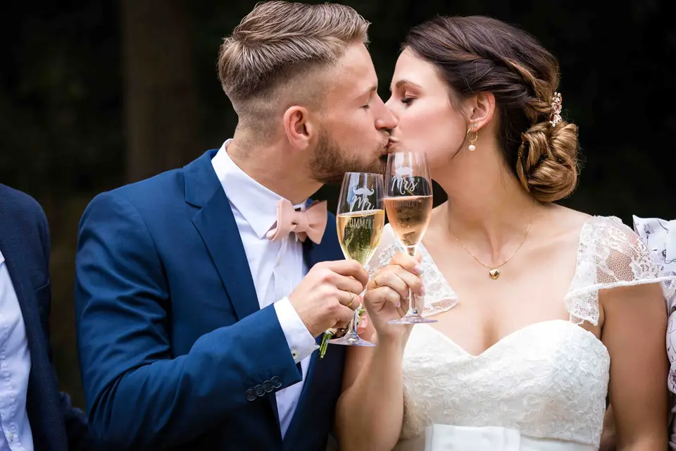 Brautpaar stößt mit Sekt an und küsst sich