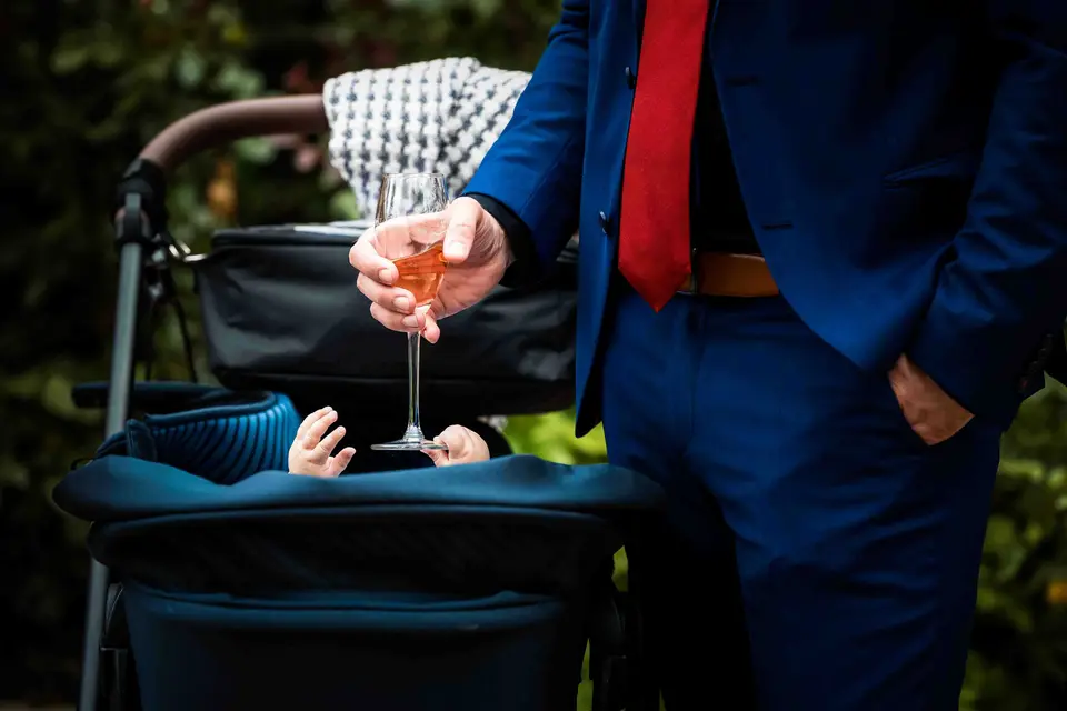 Kleines Kind im Kinderwagen greift nach einem Sektglas