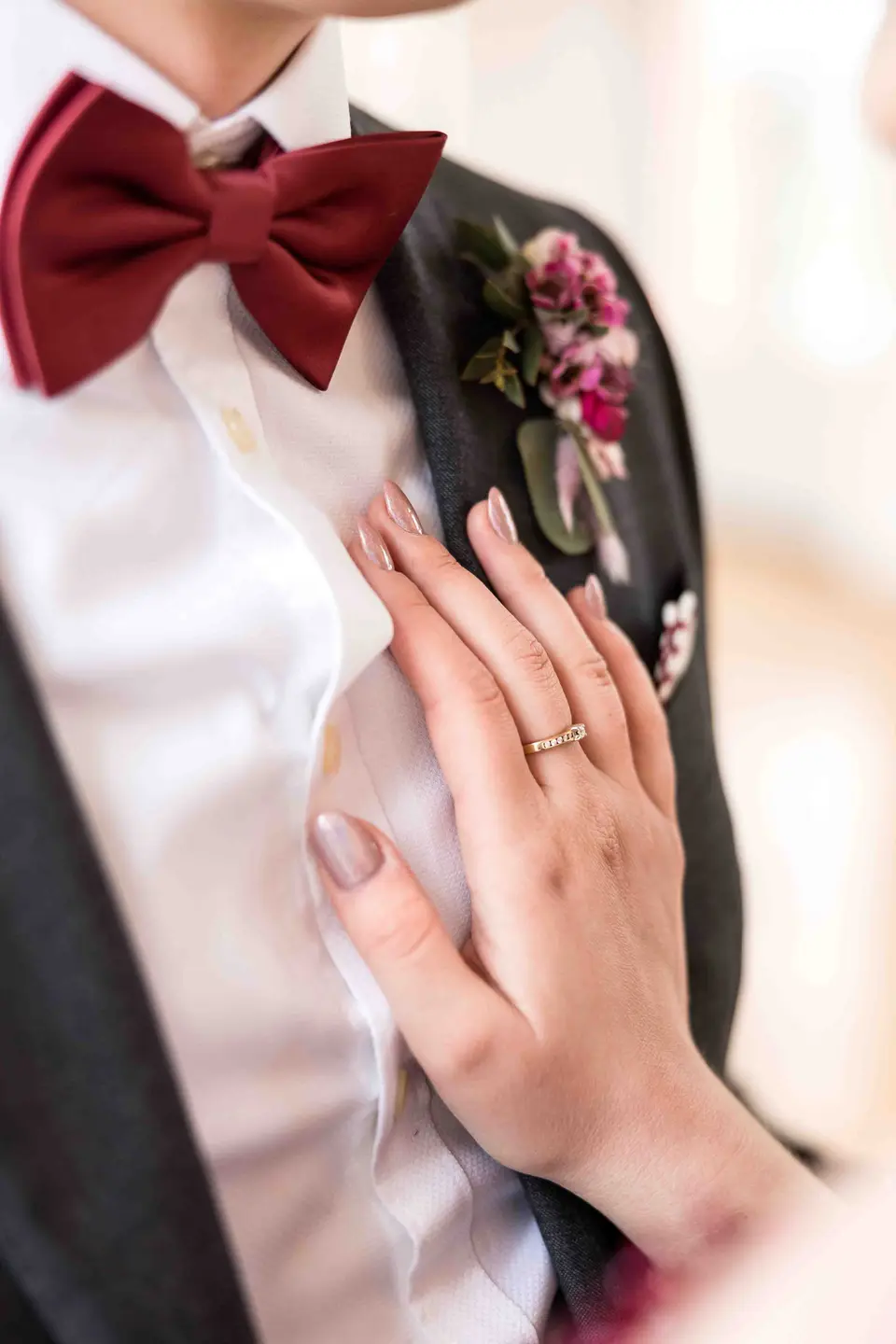 Hand der Braut mit Ring auf der Brust des Bräutigams mit roter Fliege