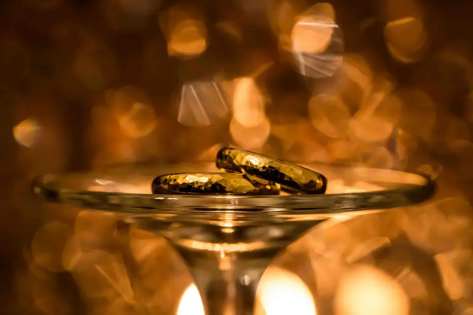 Goldene Eheringe auf einer Glasschale vor warmem Lichterglanz