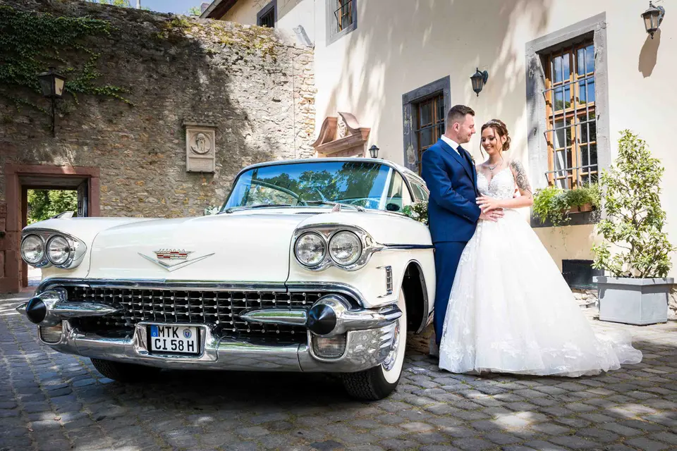 Brautpaar neben einem weißen Oldtimer vor dem Standesamt