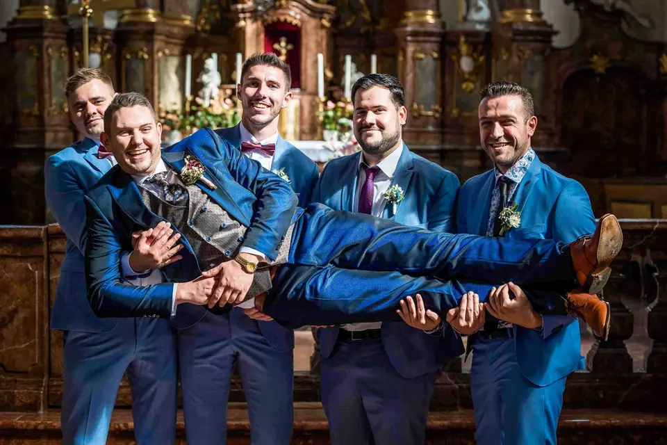 Trauzeugen in blauen Anzügen tragen den Bräutigam vor dem Altar