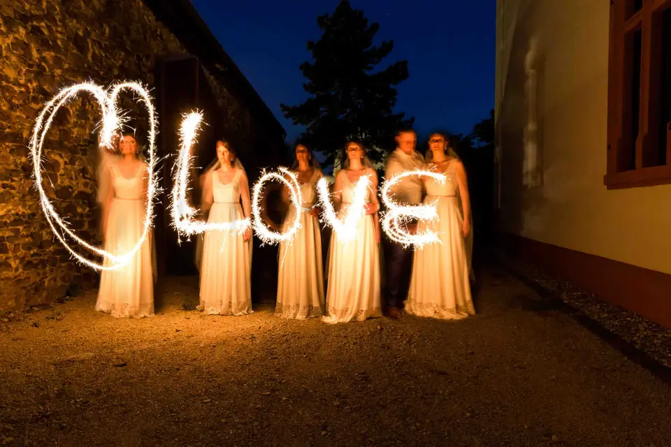 Frauen in hellen Kleidern schreiben mit Wunderkerzen ein Herz und Love