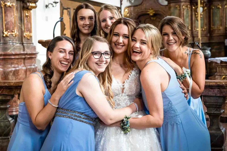 Braut umarmt lachend ihre Brautjungfern für ein Gruppenbild in der Kirche