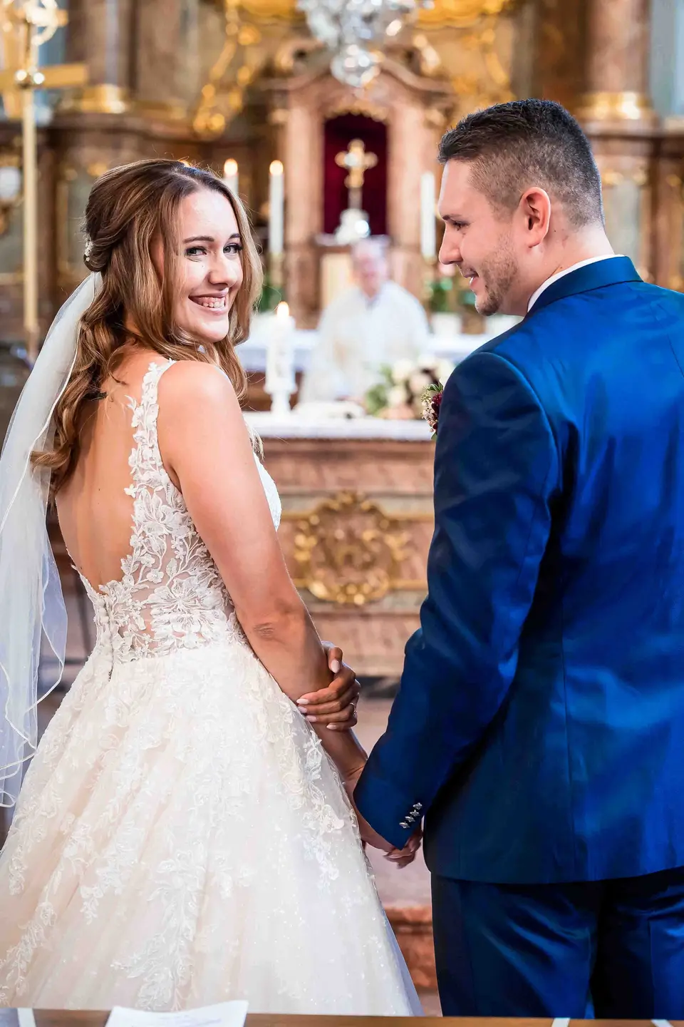 Braut blickt lächelnd über die Schulter, Brautpaar Hand in Hand am Altar